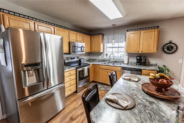 kitchen featuring a skylight, a sink, stainless steel appliances, light wood-style floors, and a textured ceiling