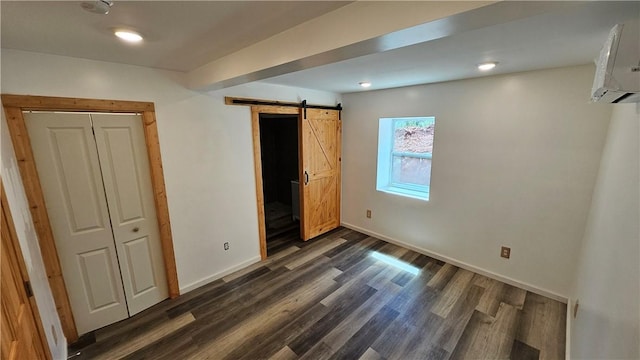 unfurnished bedroom with a barn door, baseboards, dark wood-style flooring, and a wall mounted AC