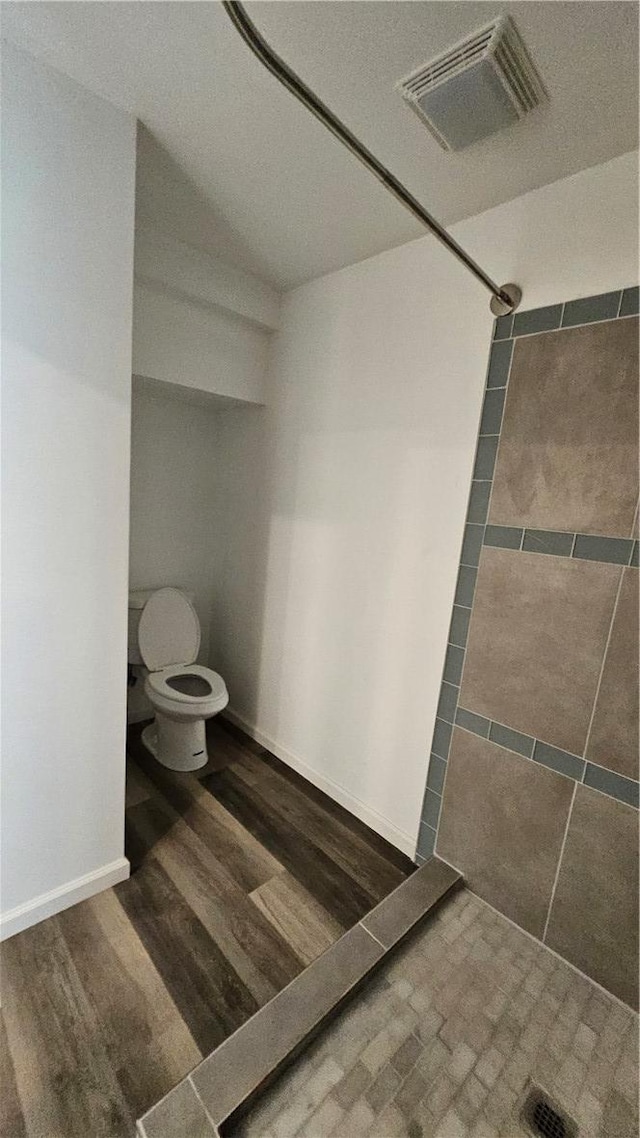 full bathroom featuring visible vents, toilet, wood finished floors, baseboards, and tiled shower