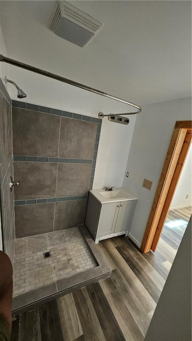 full bathroom featuring visible vents, tiled shower, vanity, and wood finished floors