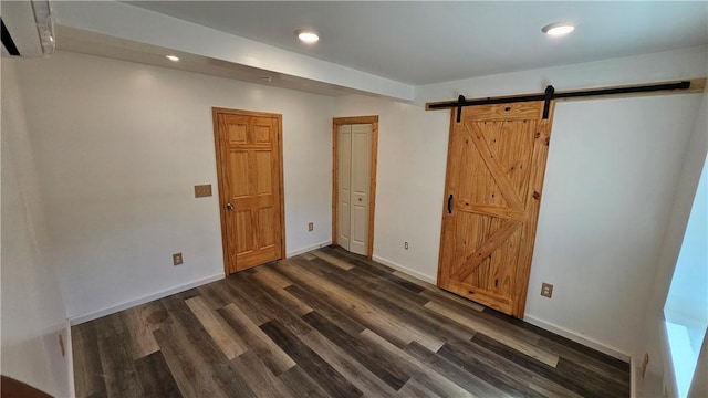 interior space with a barn door, a wall unit AC, baseboards, and dark wood-type flooring