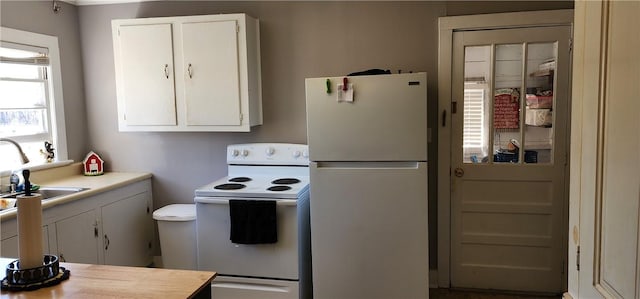 kitchen featuring white appliances, white cabinetry, light countertops, and a sink