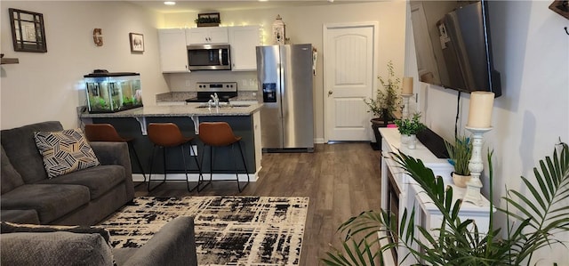 kitchen with open floor plan, a breakfast bar, light stone counters, appliances with stainless steel finishes, and dark wood-style flooring