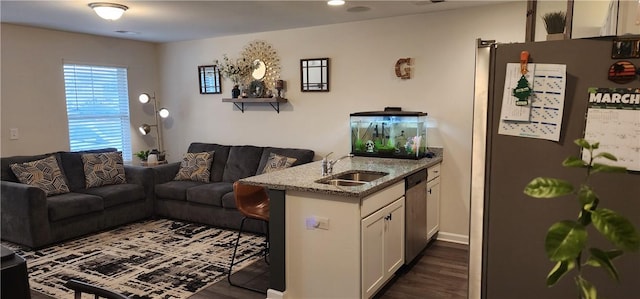 kitchen featuring light stone counters, a sink, white cabinets, appliances with stainless steel finishes, and open floor plan