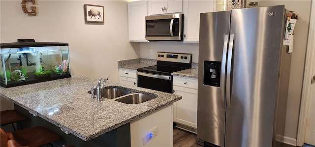 kitchen featuring a breakfast bar, a sink, light stone counters, appliances with stainless steel finishes, and white cabinets