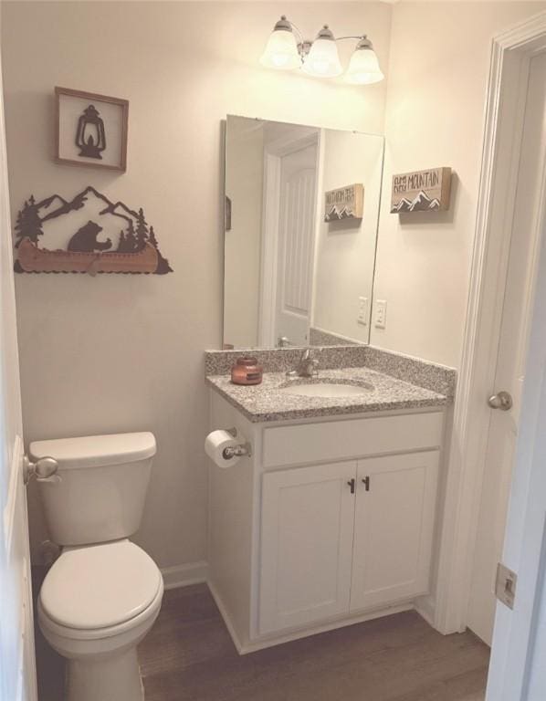 bathroom with baseboards, toilet, wood finished floors, and vanity