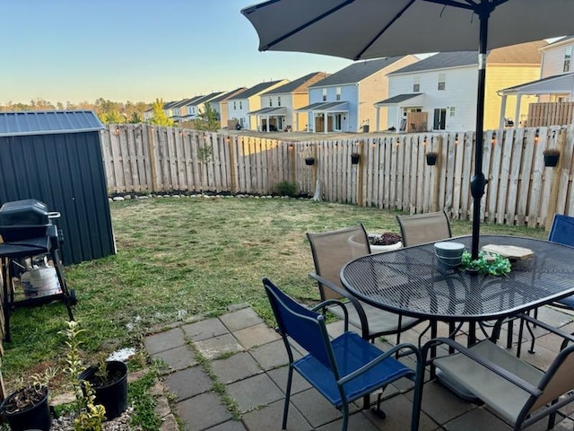 view of patio with an outbuilding, outdoor dining space, a fenced backyard, a shed, and a residential view