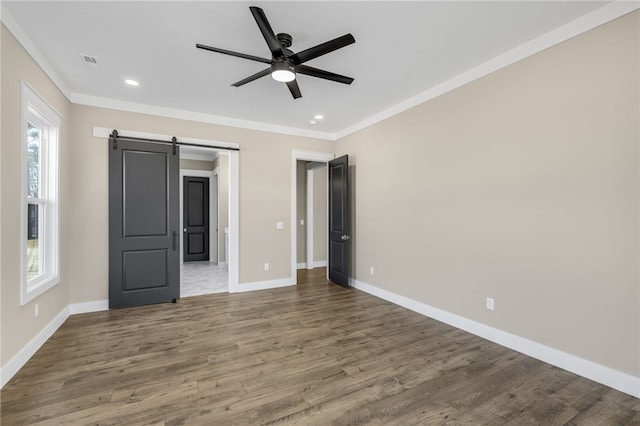 unfurnished bedroom featuring a barn door, wood finished floors, crown molding, and visible vents