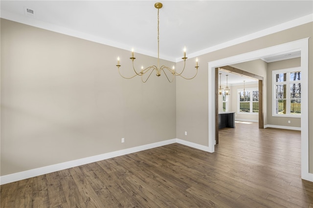 empty room with visible vents, a notable chandelier, dark wood-style floors, crown molding, and baseboards