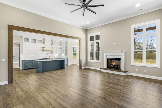 unfurnished living room featuring baseboards, dark wood-type flooring, a lit fireplace, and a ceiling fan