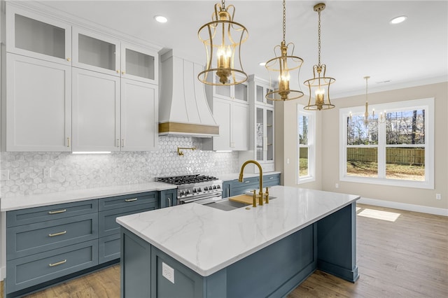 kitchen featuring a chandelier, an island with sink, custom range hood, decorative backsplash, and hanging light fixtures