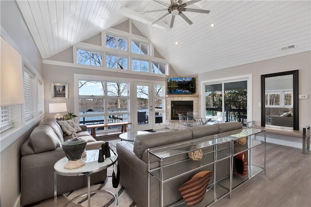 living area featuring wood finished floors, visible vents, high vaulted ceiling, ceiling fan, and a stone fireplace