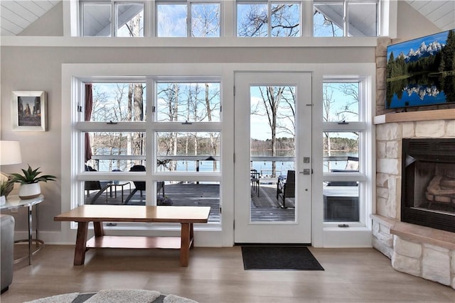 entryway featuring high vaulted ceiling, a stone fireplace, and wood finished floors