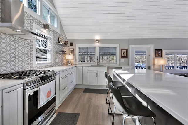 kitchen with wall chimney range hood, light countertops, gas stove, white cabinetry, and a sink