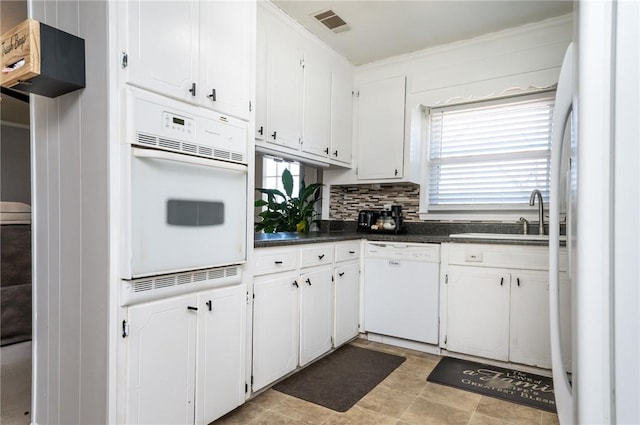 kitchen featuring dark countertops, white cabinets, white appliances, and a sink