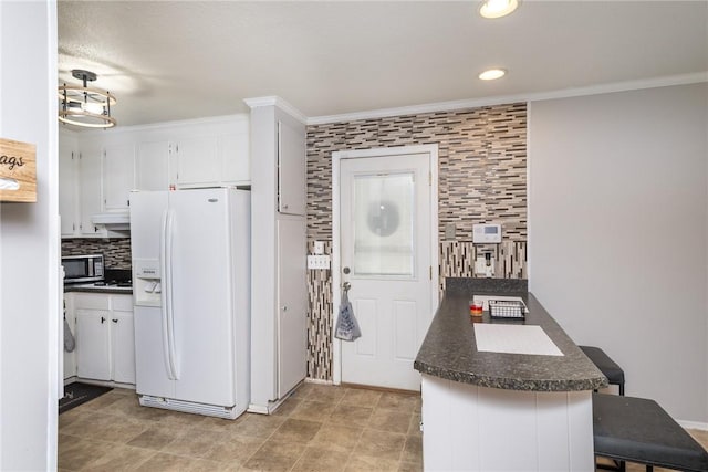 kitchen featuring stainless steel microwave, tasteful backsplash, dark countertops, white refrigerator with ice dispenser, and white cabinets