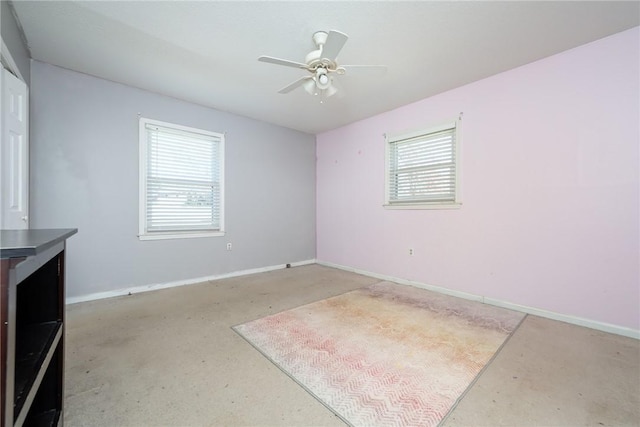 empty room with plenty of natural light, ceiling fan, concrete flooring, and baseboards