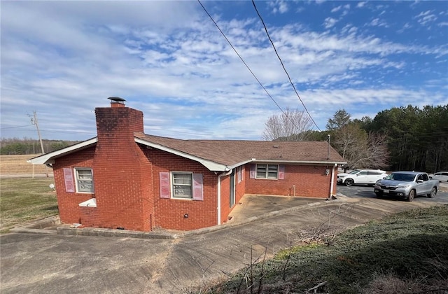 view of home's exterior featuring brick siding, driveway, a chimney, and roof with shingles