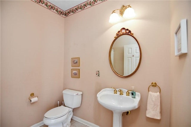 half bath featuring tile patterned floors, toilet, baseboards, and a sink