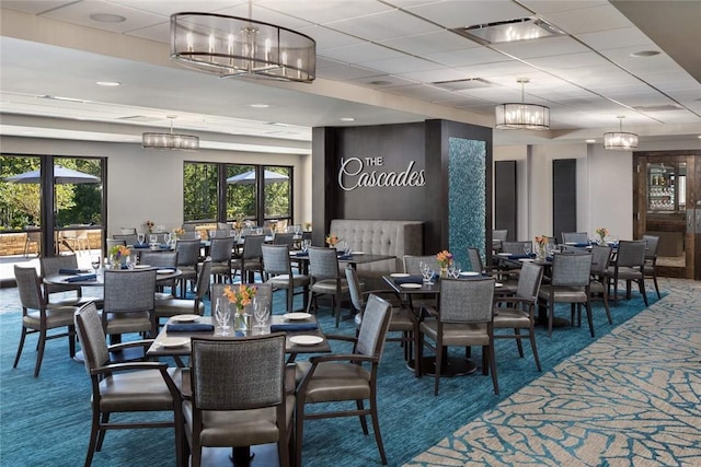 dining space with carpet flooring, visible vents, a paneled ceiling, and an inviting chandelier