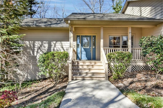 doorway to property with a porch and a shingled roof