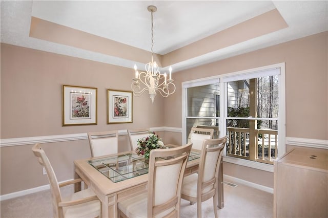 carpeted dining space featuring a tray ceiling, baseboards, and an inviting chandelier