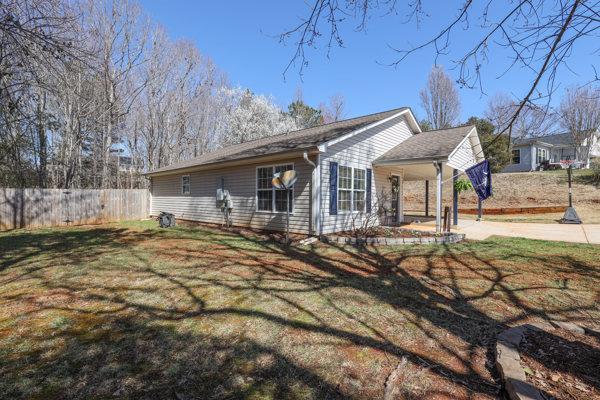 view of side of property with an attached carport, a lawn, and fence