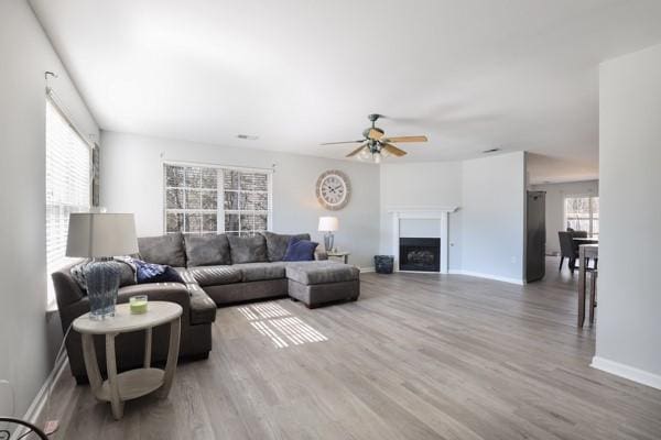 living area featuring a fireplace, baseboards, a ceiling fan, and wood finished floors