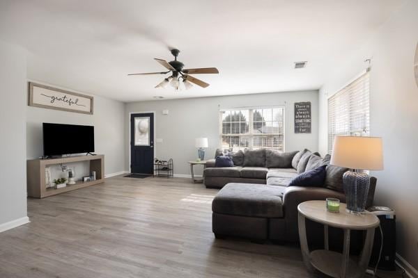 living room featuring wood finished floors, a ceiling fan, visible vents, and baseboards