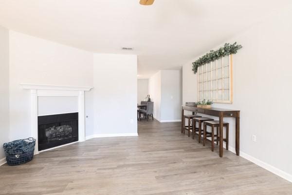 living room featuring a fireplace, wood finished floors, visible vents, and baseboards