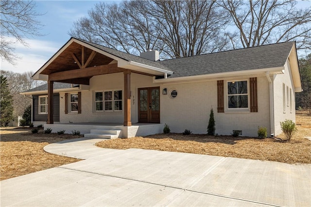 view of front of property with brick siding, a porch, roof with shingles, french doors, and a chimney