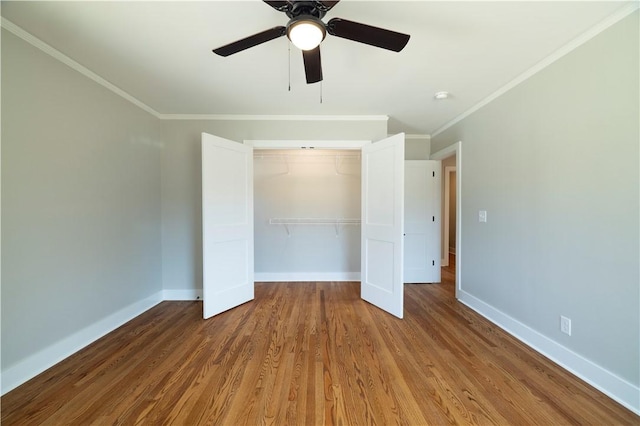 unfurnished bedroom featuring crown molding, wood finished floors, baseboards, and a closet