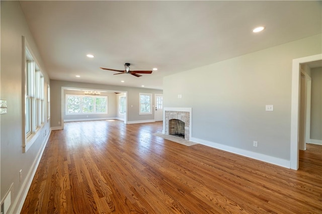 unfurnished living room featuring a brick fireplace, baseboards, ceiling fan, and wood finished floors