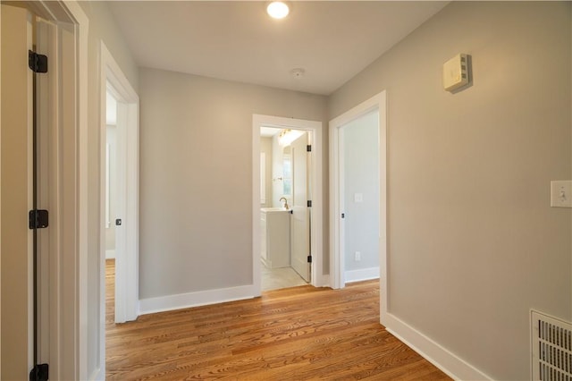 corridor featuring visible vents, light wood-type flooring, baseboards, and a sink