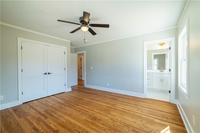 unfurnished bedroom featuring light wood finished floors, connected bathroom, baseboards, ornamental molding, and a closet