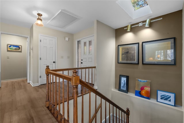 hall featuring wood finished floors, a skylight, an upstairs landing, and baseboards