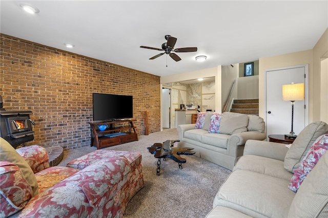 carpeted living area with stairway, brick wall, a wood stove, and a ceiling fan