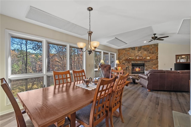 dining space featuring ceiling fan with notable chandelier, vaulted ceiling, a stone fireplace, and wood finished floors