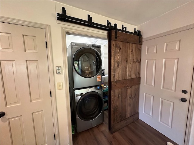 clothes washing area with laundry area, stacked washer / dryer, a barn door, and dark wood-style flooring