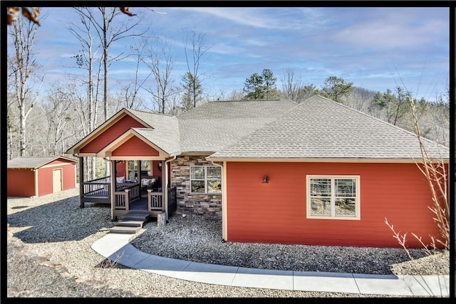 view of front of house featuring a shed, roof with shingles, an outdoor structure, stone siding, and a deck