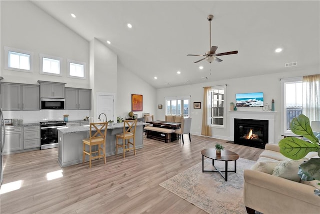 living room with ceiling fan, plenty of natural light, visible vents, and light wood-type flooring