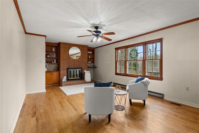 living room featuring visible vents, light wood-style flooring, ornamental molding, a baseboard heating unit, and ceiling fan