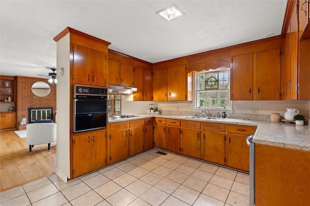 kitchen with black oven, cooktop, under cabinet range hood, light countertops, and a sink