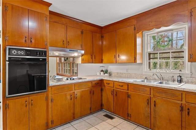 kitchen with oven, under cabinet range hood, light countertops, stainless steel cooktop, and a sink