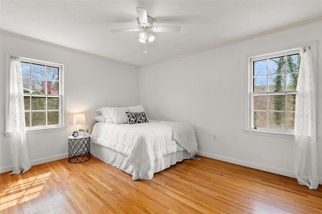 bedroom with multiple windows, baseboards, light wood-style floors, and ornamental molding