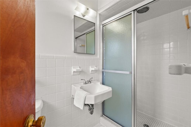 bathroom featuring a wainscoted wall, toilet, a stall shower, and tile walls