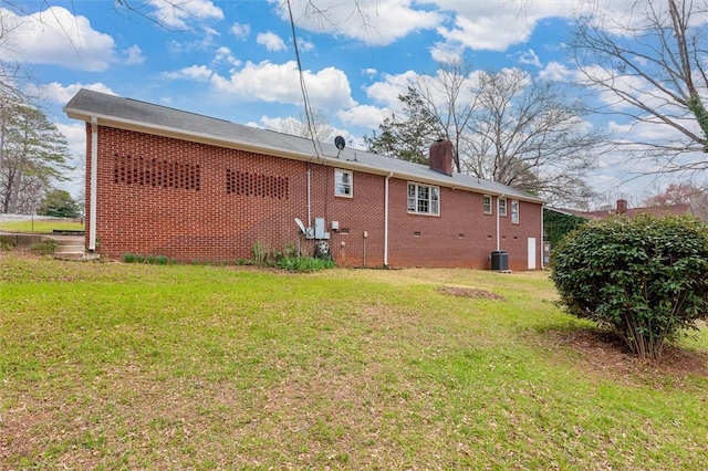 rear view of property featuring brick siding, a chimney, and a yard