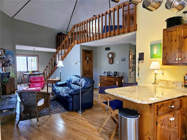 kitchen with light wood-type flooring, high vaulted ceiling, light stone counters, open floor plan, and brown cabinetry