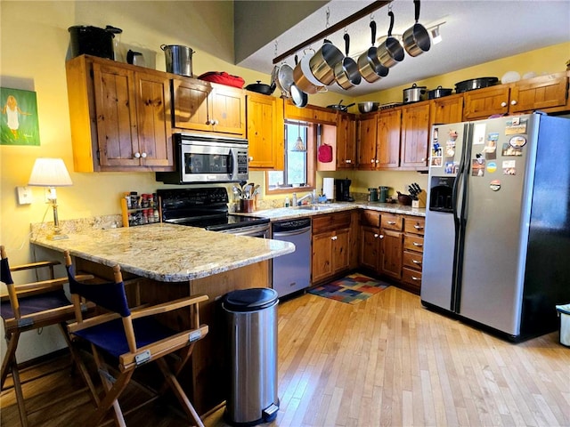 kitchen featuring light wood-style flooring, stainless steel appliances, a peninsula, a breakfast bar area, and brown cabinetry