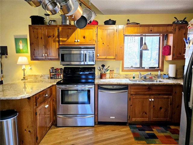 kitchen featuring light wood finished floors, a peninsula, a sink, appliances with stainless steel finishes, and brown cabinets